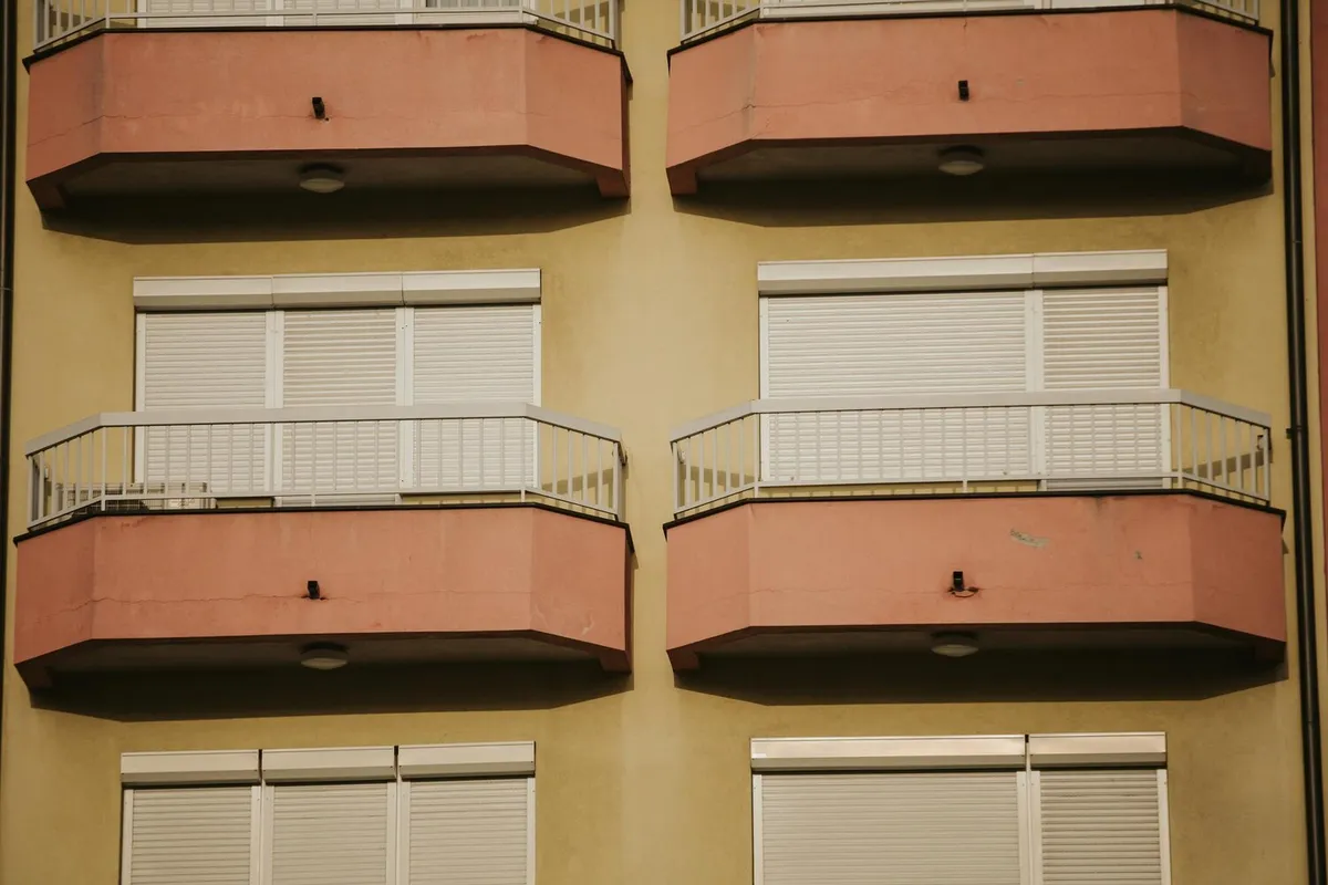 Façade d'immeuble méditerranéen avec balcons et volets roulants blancs baissés